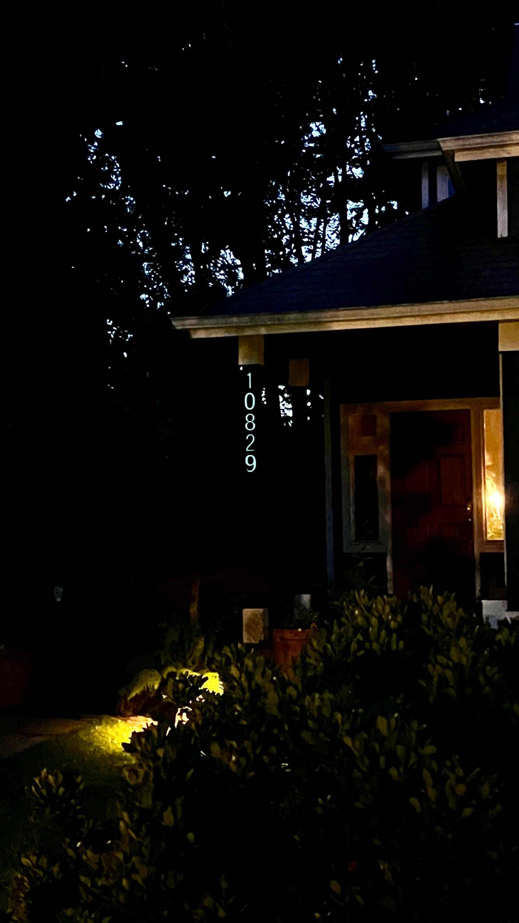 Nighttime view of a house with glow-in-the-dark numbers, brightly illuminated in a soft blue hue. The numbers are mounted on a brick wall, making them clearly visible and adding a touch of modern elegance to the home's exterior.